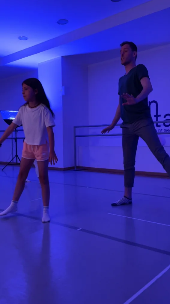 Una alumna y el profesor en un ejercicio de movimiento bajo luz azul en una clase de teatro